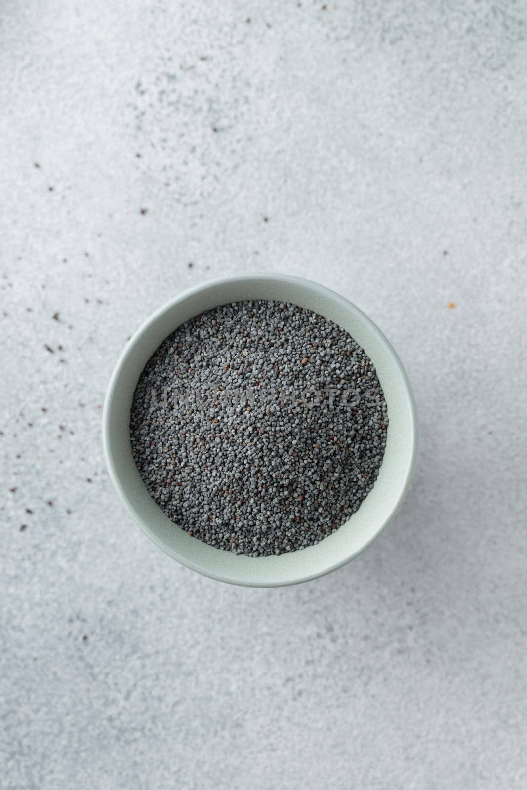 Bowl with poppy seeds on concrete background top view