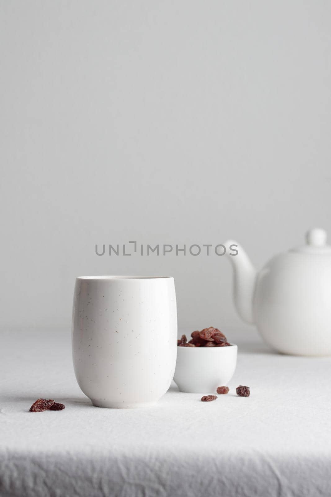 White teacup with raisins and teapot on a white background