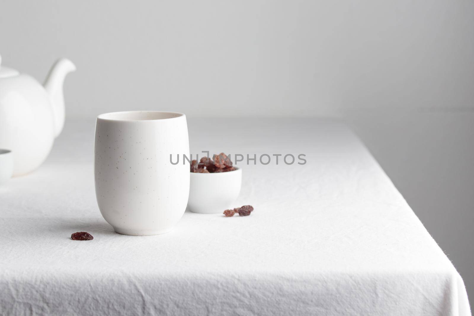 White teacup with raisins and teapot on a white background