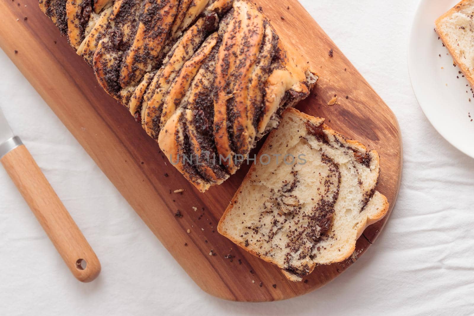 Piece of swirl homemade bread with poppy seeds on a white table