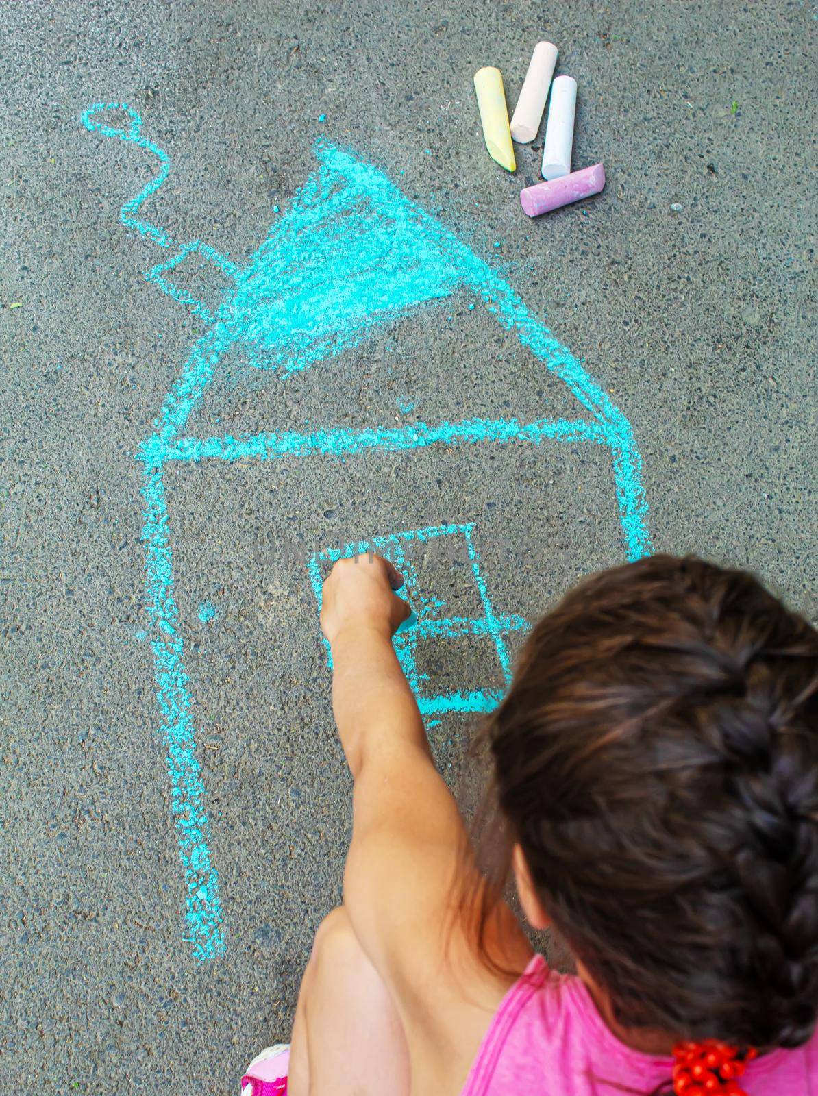 The child draws the house with chalk on the asphalt. Selective focus. draw.