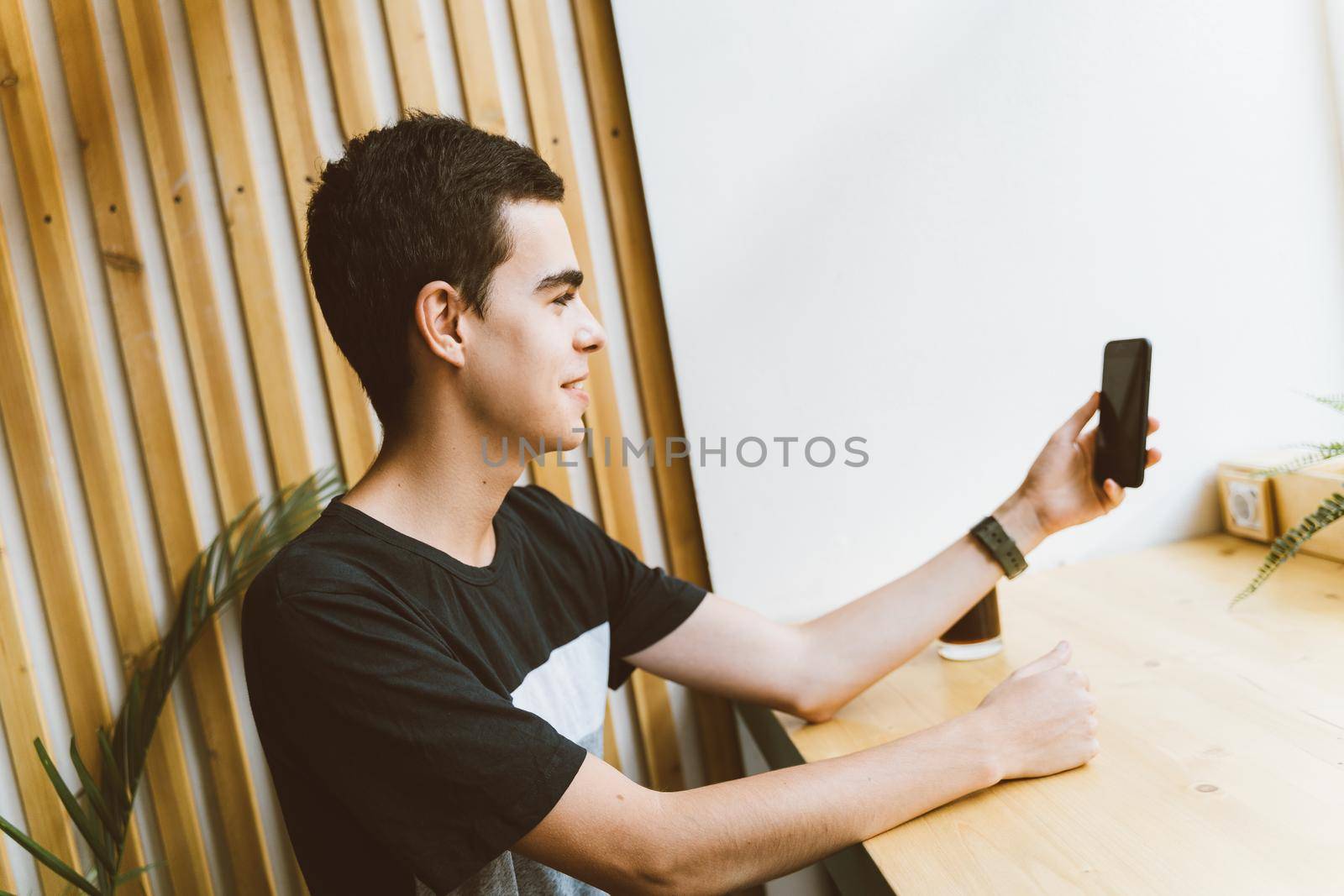 The young man looks at the phone, smiling. Takes a selfie. Teenager talking in chat. The blogger communicates online, broadcasts, copy space