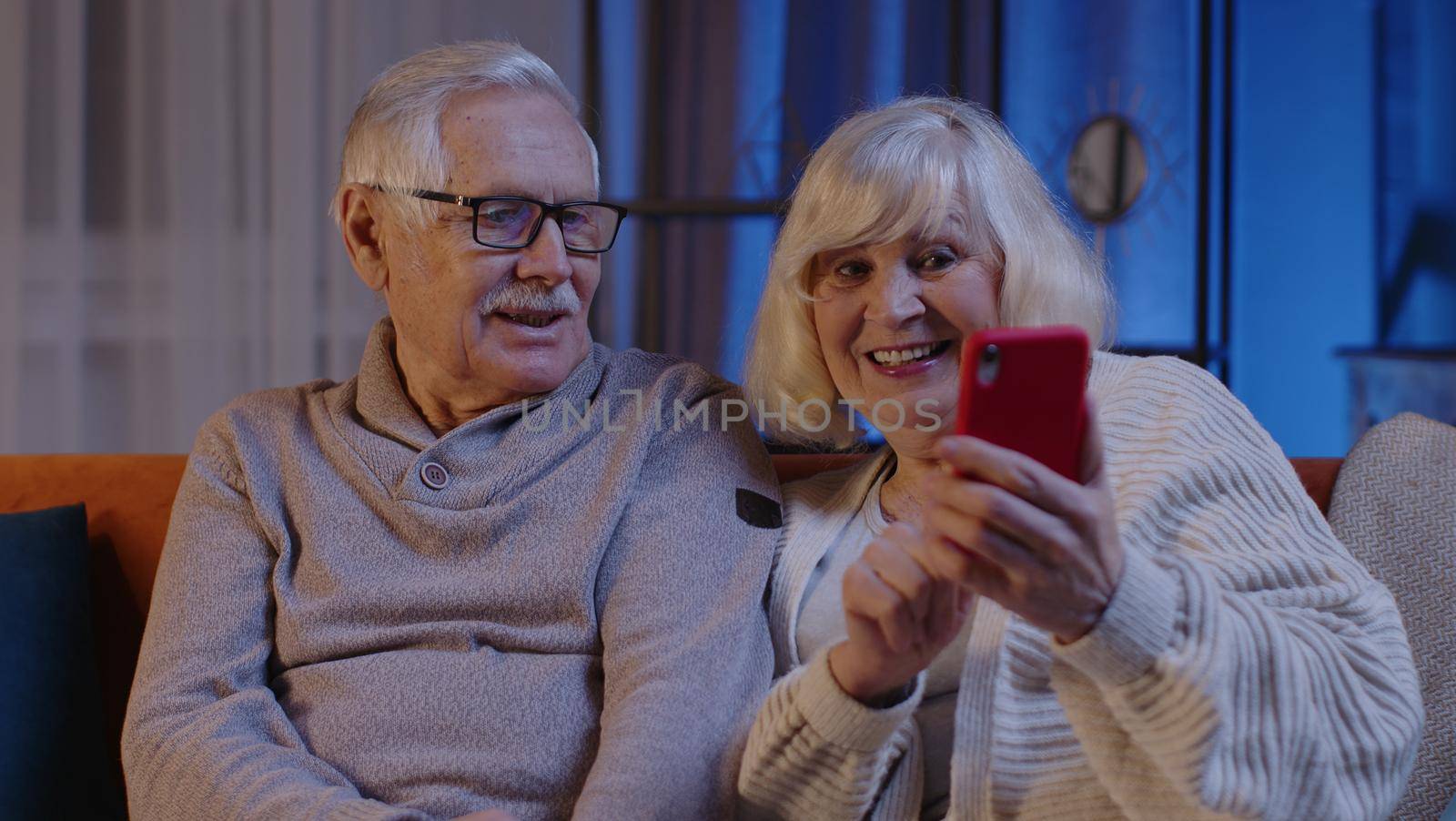 Mature Grandmother Grandfather Making Video Call Online On Mobile Phone At Home Sofa. Senior Old Couple Grandparents Having Conversation Webcam Chat. Happy Old Family Using Smartphone. 6k Downscale