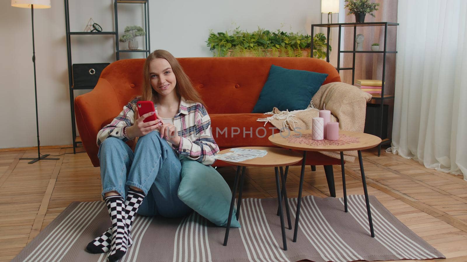 Smiling happy young woman counting money cash and use mobile phone calculate domestic bills at home by efuror