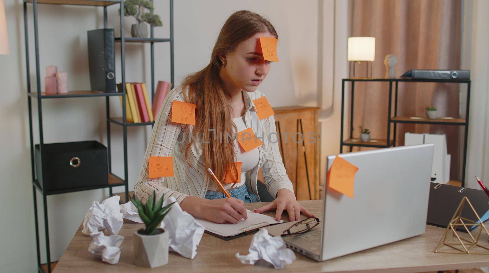 Exhausted woman freelancer with pasted sticker notes using laptop computer having concentration problem, creative crisis. Nervous adult girl confused by big routine work loading indoors at home office