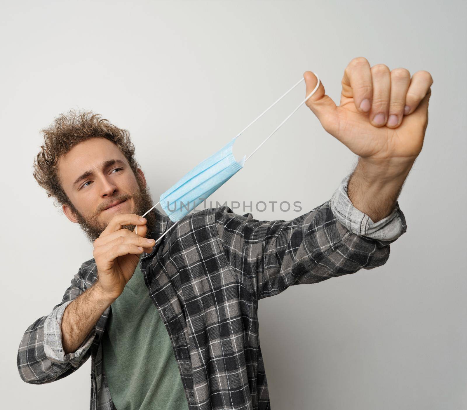Tired of face mask young man in plaid shirt pops it in the air. Happy handsome anti mask guy. Exhausted young man trying to rid of medical mask. Health care concept. Covid 19 concept.