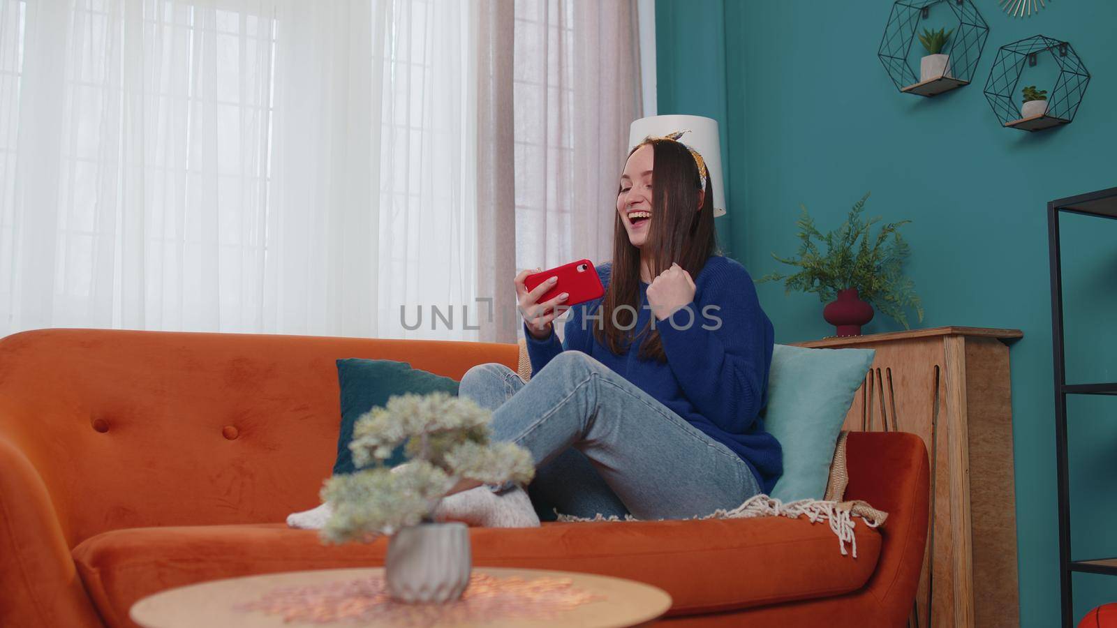 Worried funny addicted woman enthusiastically playing racing video games on mobile phone at home in living room on sofa. Young adult teen girl using smartphone gadget app with drive simulator isolated