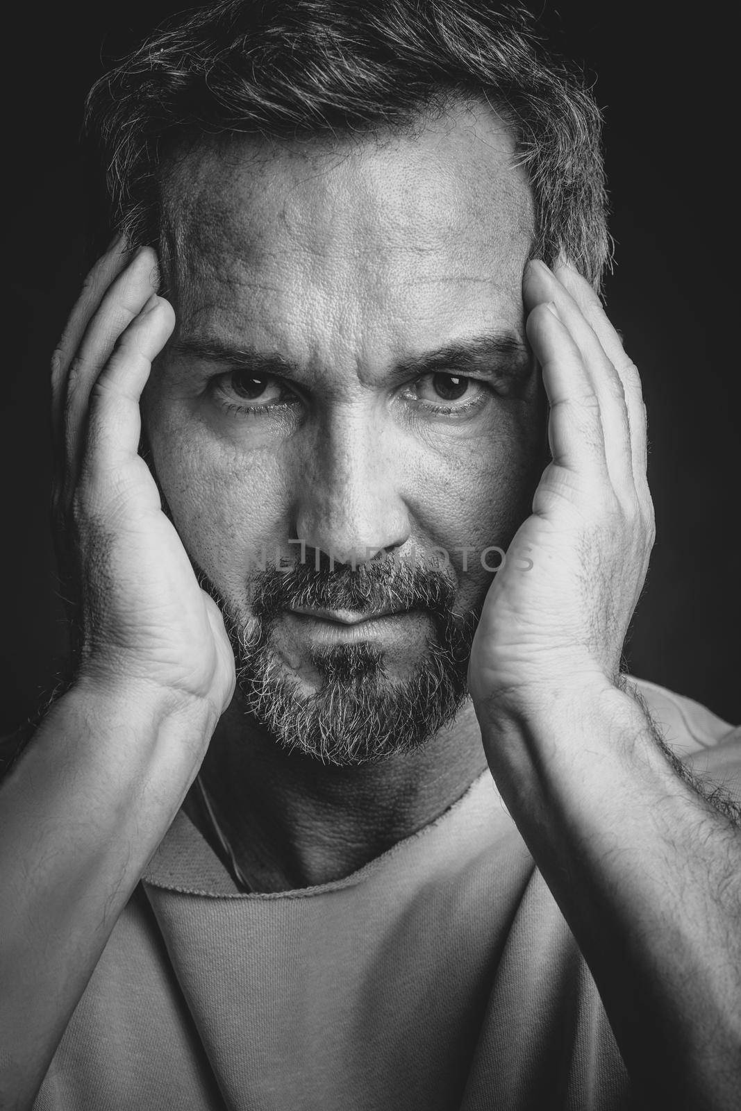 Middle aged grey haired man hold his face with hands looking at camera. Handsome middle aged man in black and white photo. Black and white portrait of attractive, beautiful, serious man.