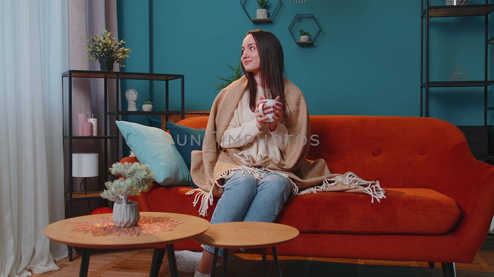 Portrait of smiling young brunette woman in warm white sweater drink hot beverage mug relaxing at winter home morning. Happy female posing with tea coffee cup having positive emotion at cozy interior
