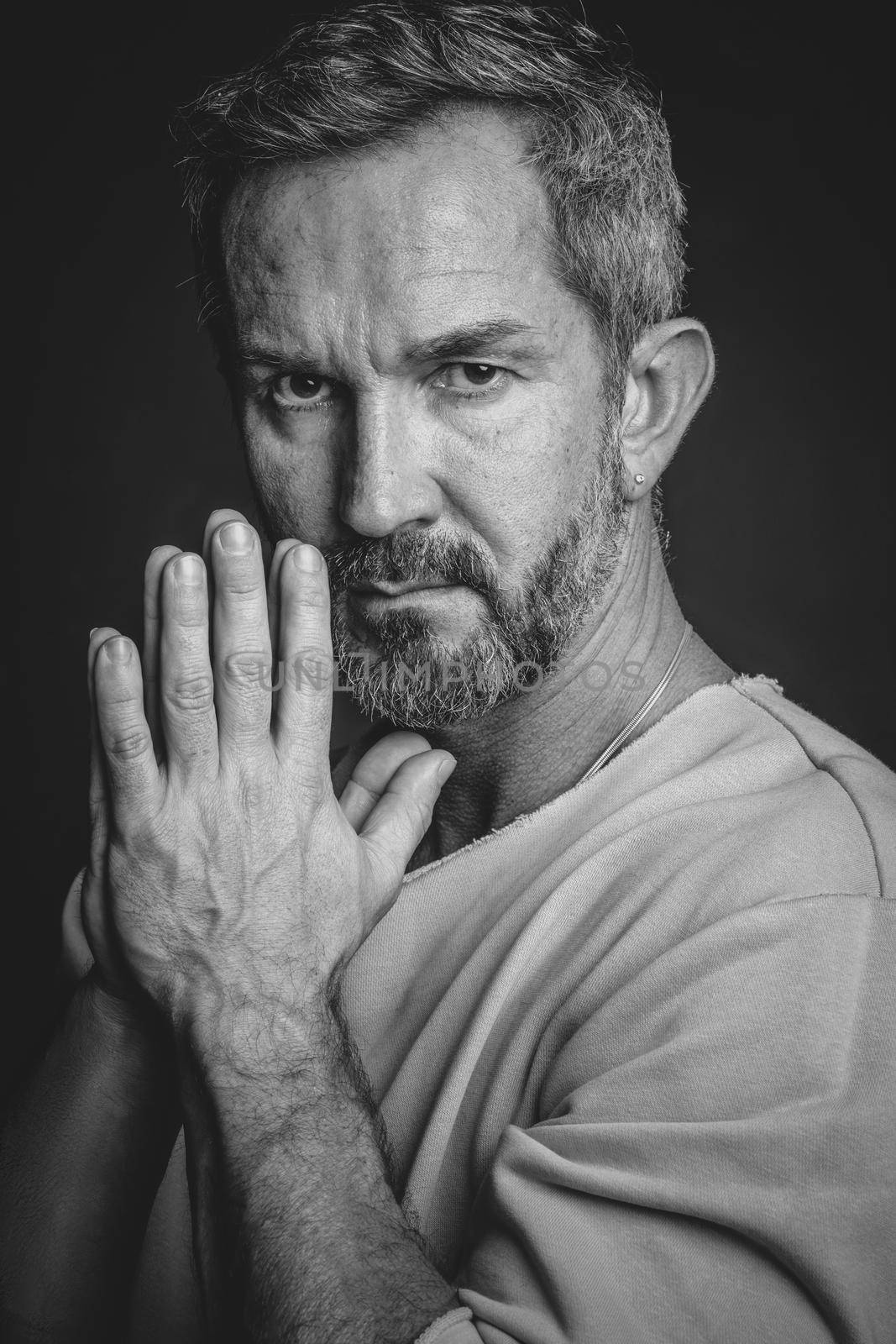 Grey haired mature man put hands together looking at camera. Handsome middle aged man in black and white photo. Black and white portrait of attractive, beautiful, serious man.