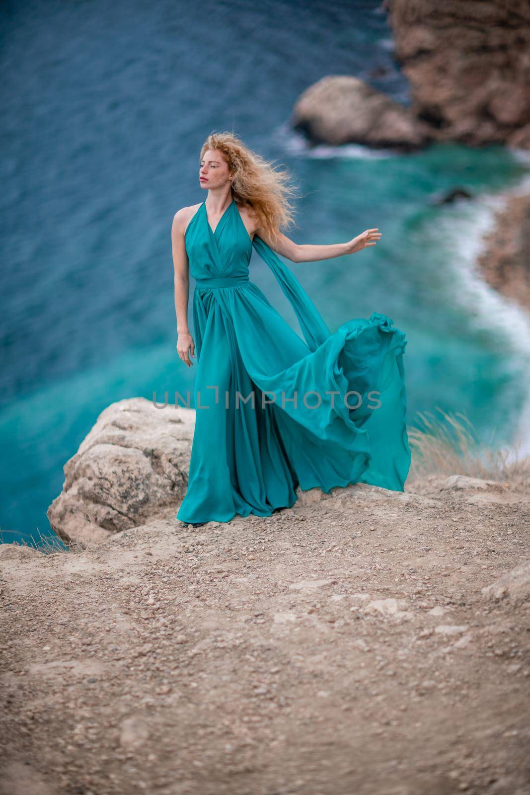 A woman in an emerald dress, a fashion model with long silk wings in a flowing dress, flying fabric on the embankment