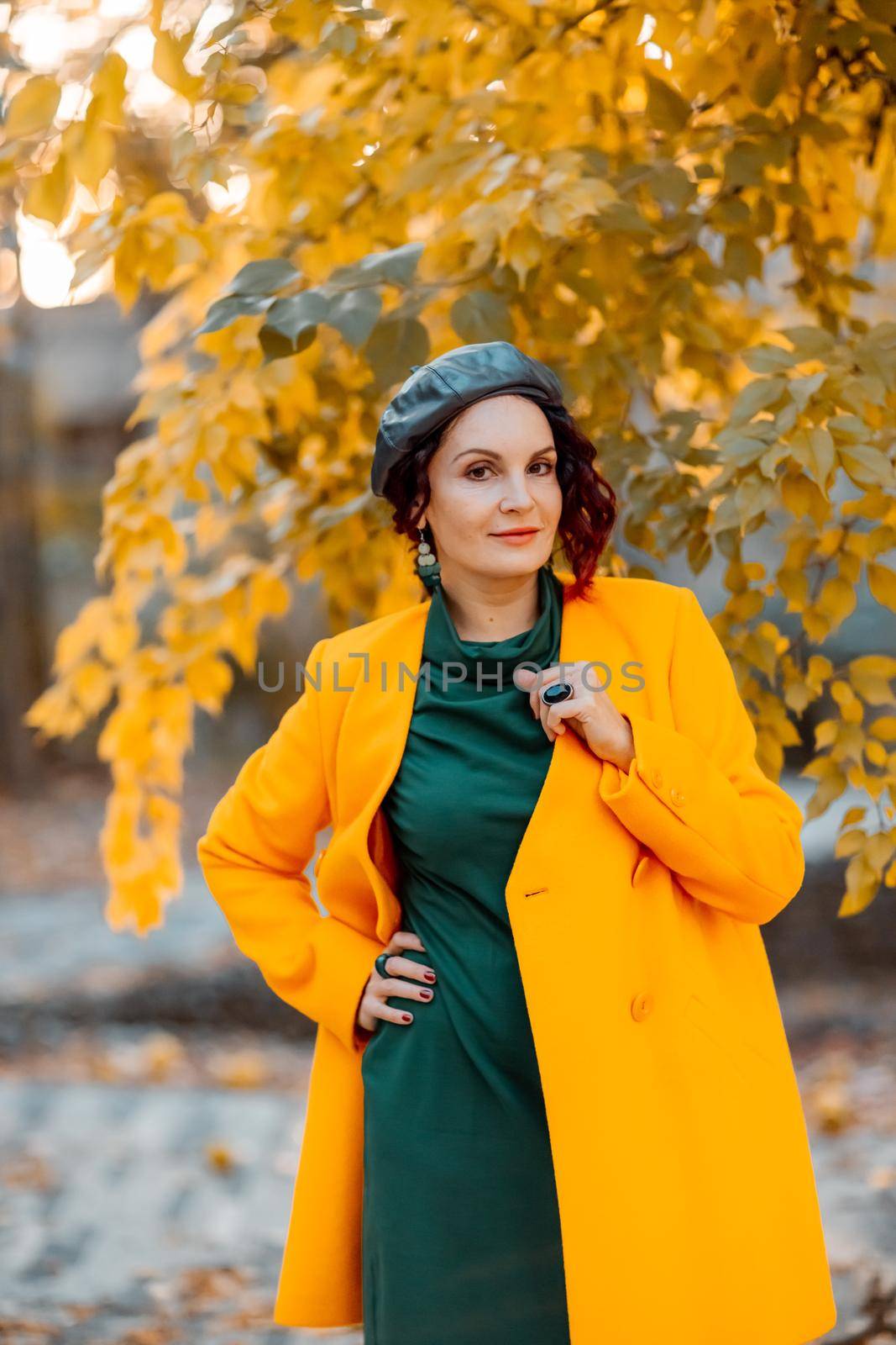 Beautiful woman walks outdoors in autumn. She is wearing a yellow coat and a green dress. Young woman enjoying the autumn weather. Autumn content