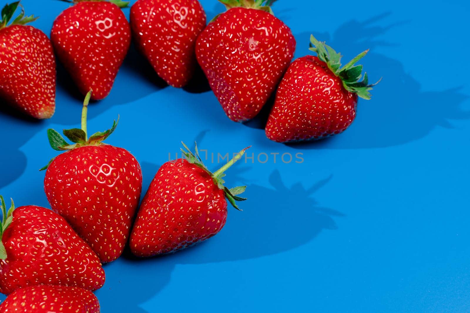 Bunch of strawberries on blue background. Red berry summer seasonal fruit