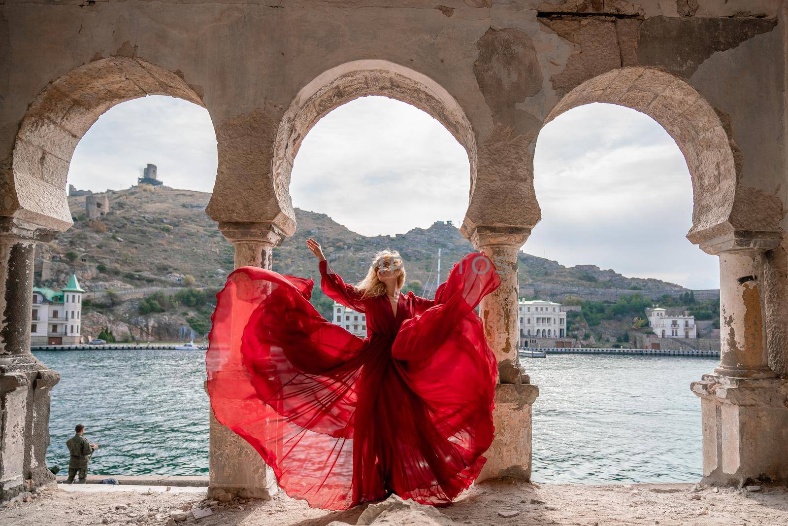 View of Balaklava Bay through an arched balcony in oriental style. The girl in a long red dress stands with her back. Abandoned mansion on the Black Sea coast.