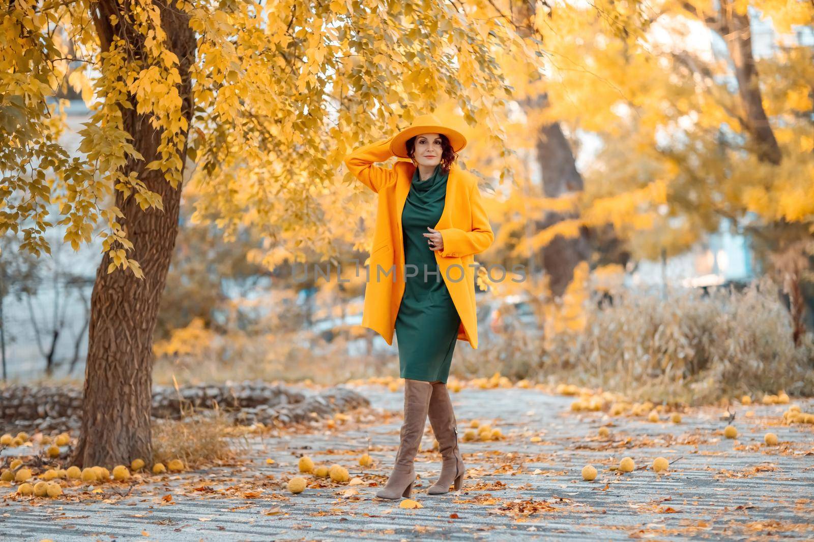Beautiful woman walks outdoors in autumn. She is wearing a yellow coat, yellow hat and green dress. Young woman enjoying the autumn weather. Autumn content.