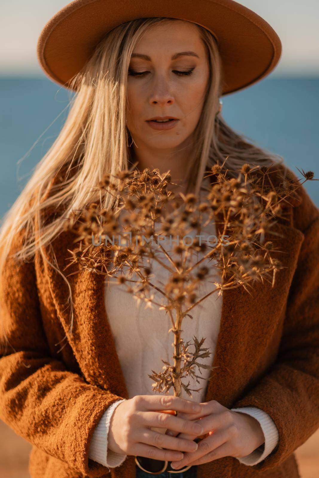 A woman walking along the coast near the sea. An elegant lady in a brown coat and a hat with fashionable makeup walks on the seashore by Matiunina