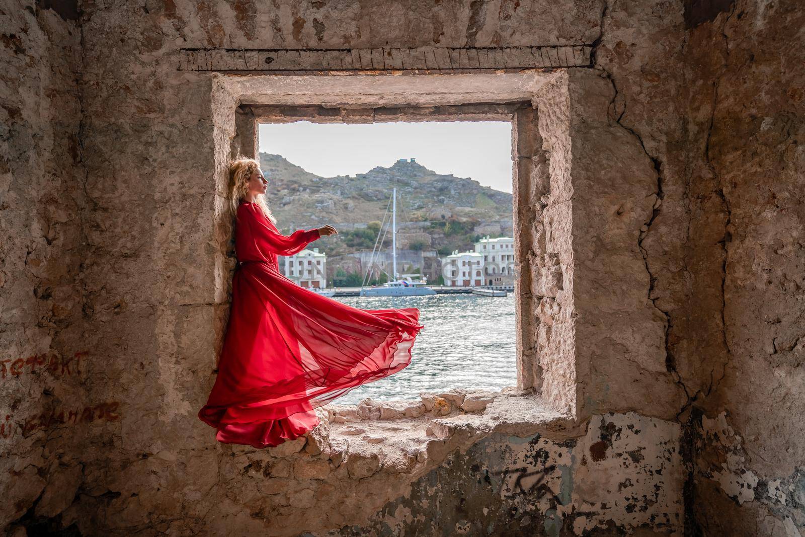 View of Balaklava Bay through an arched balcony in oriental style. The girl in a long red dress stands with her back. Abandoned mansion on the Black Sea coast by Matiunina