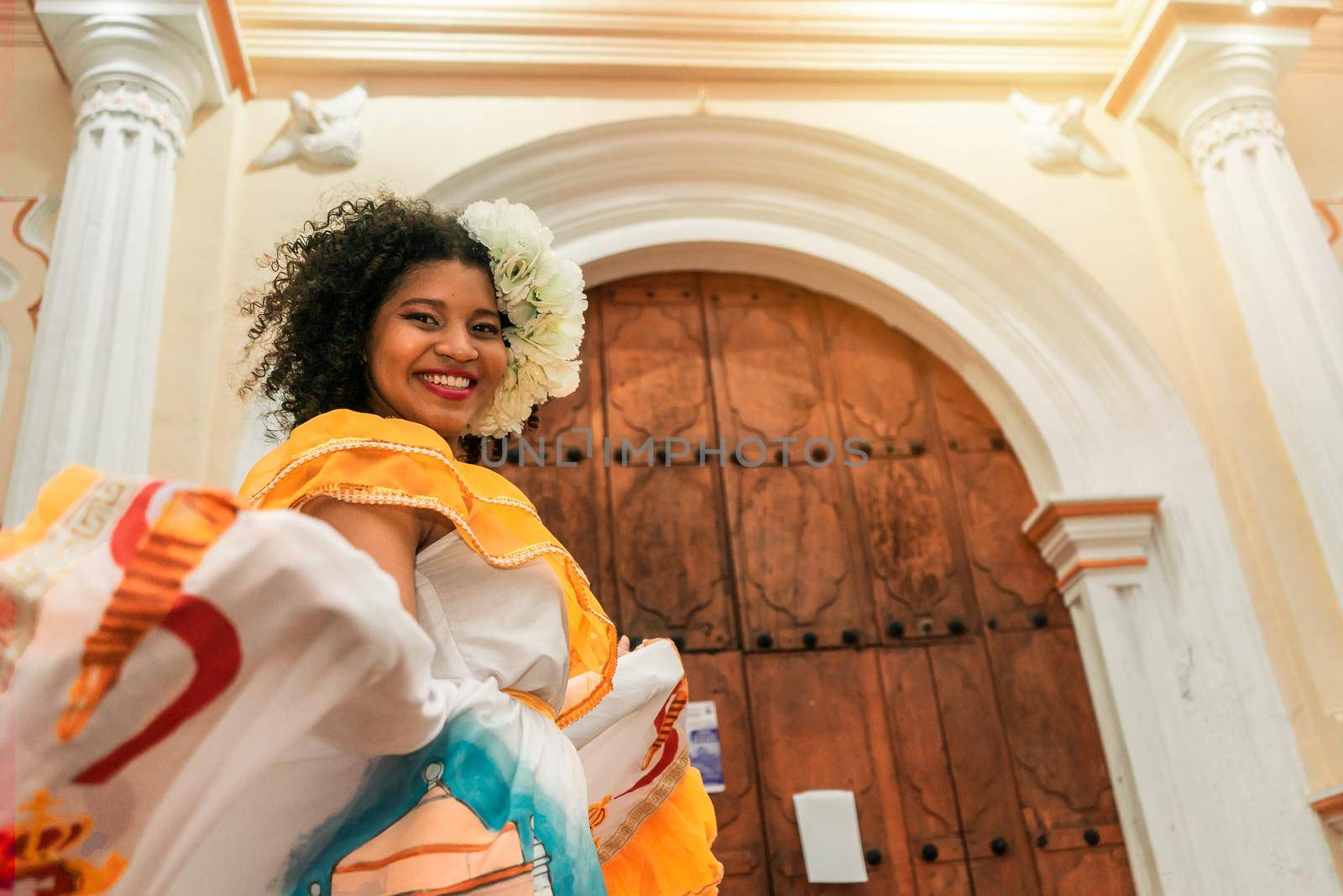 Young mestizo woman with curly black hair outside a church in Leon Nicaragua, wearing a traditional yellow dress looking at the camera and smiling. Concept of dance culture and tradition in Latin America.