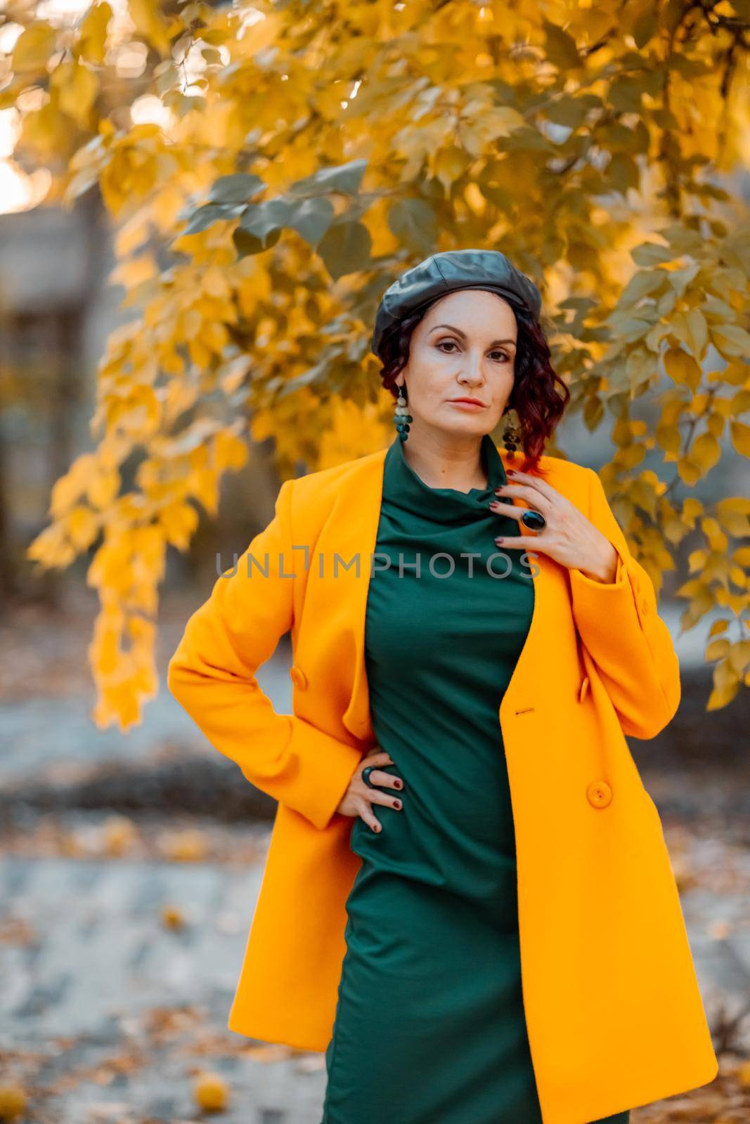 Beautiful woman walks outdoors in autumn. She is wearing a yellow coat and a green dress. Young woman enjoying the autumn weather. Autumn content