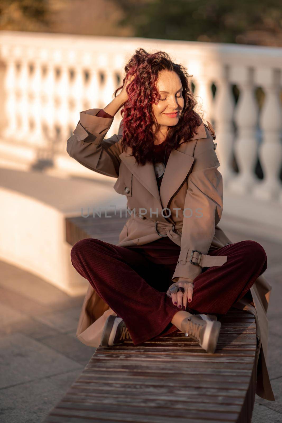 Outdoor fashion portrait of young elegant fashionable brunette woman, model in stylish hat, choker and light raincoat posing at sunset in European city