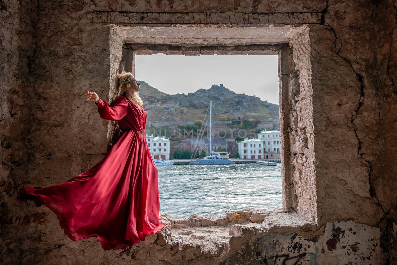 View of Balaklava Bay through an arched balcony in oriental style. The girl in a long red dress stands with her back. Abandoned mansion on the Black Sea coast.