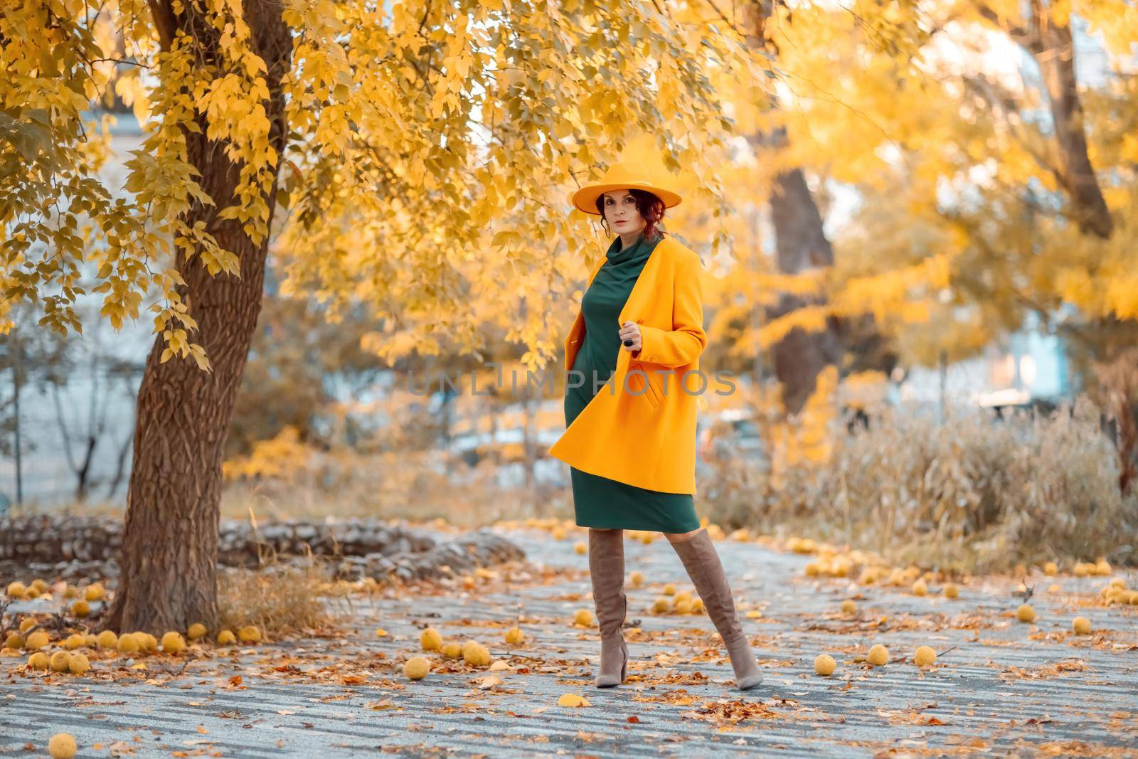 Beautiful woman walks outdoors in autumn. She is wearing a yellow coat, yellow hat and green dress. Young woman enjoying the autumn weather. Autumn content by Matiunina