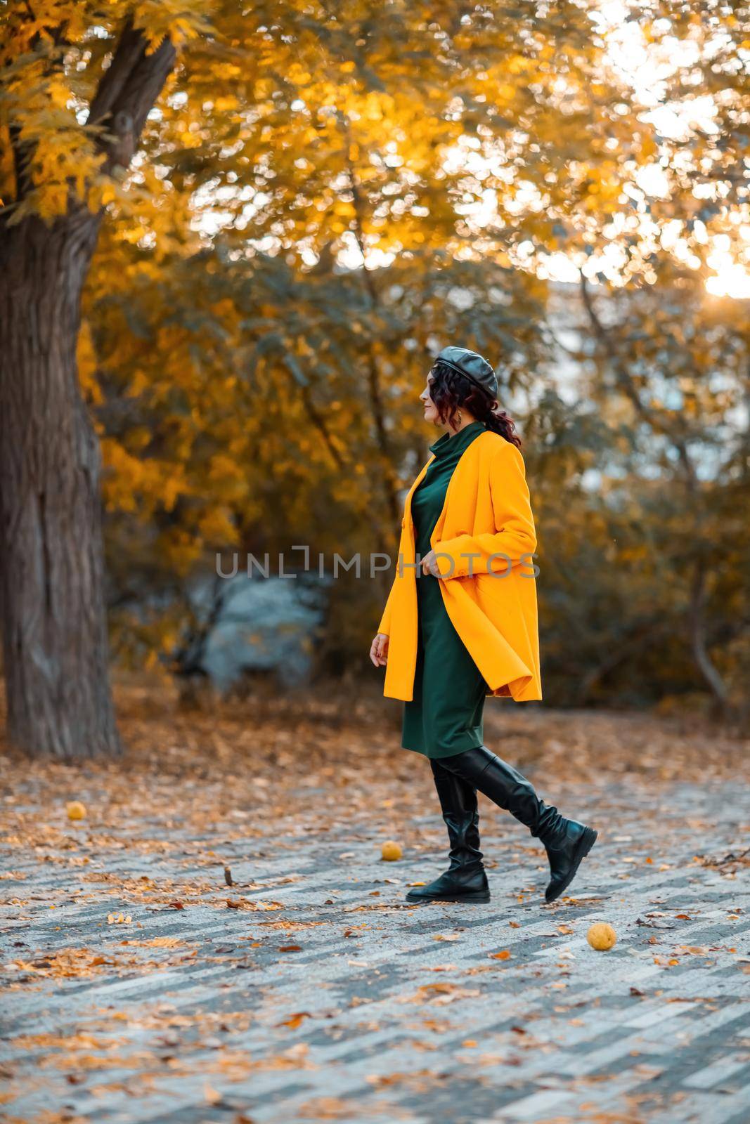 Beautiful woman walks outdoors in autumn. She is wearing a yellow coat and a green dress. Young woman enjoying the autumn weather. Autumn content. by Matiunina