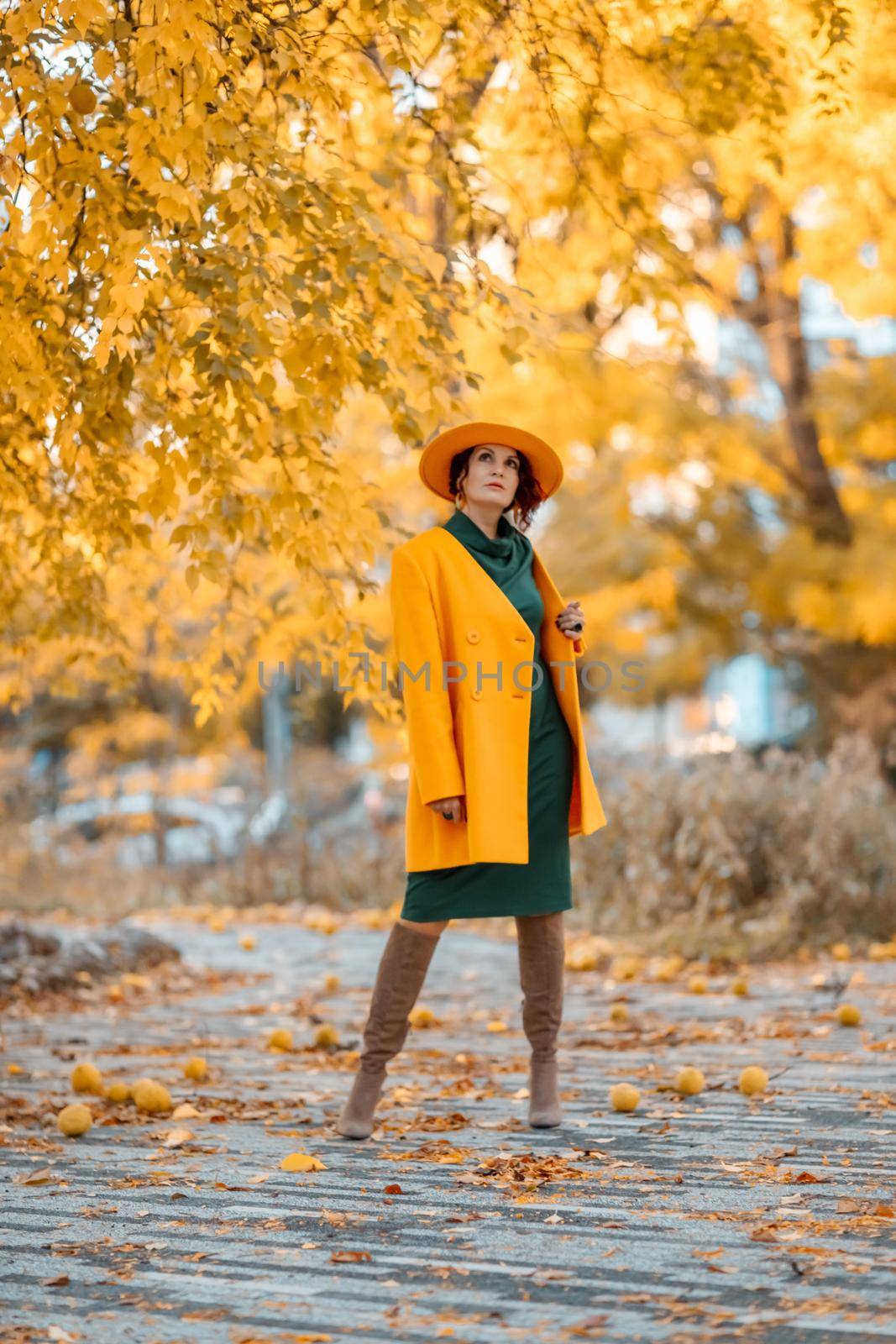 Beautiful woman walks outdoors in autumn. She is wearing a yellow coat, yellow hat and green dress. Young woman enjoying the autumn weather. Autumn content.