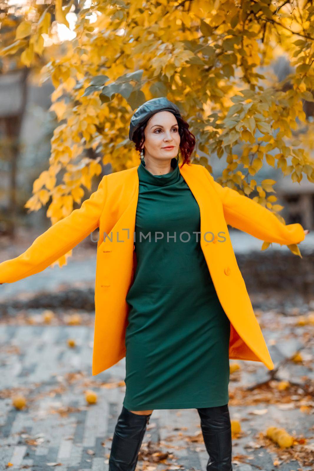 Beautiful woman walks outdoors in autumn. She is wearing a yellow coat and a green dress. Young woman enjoying the autumn weather. Autumn content. by Matiunina