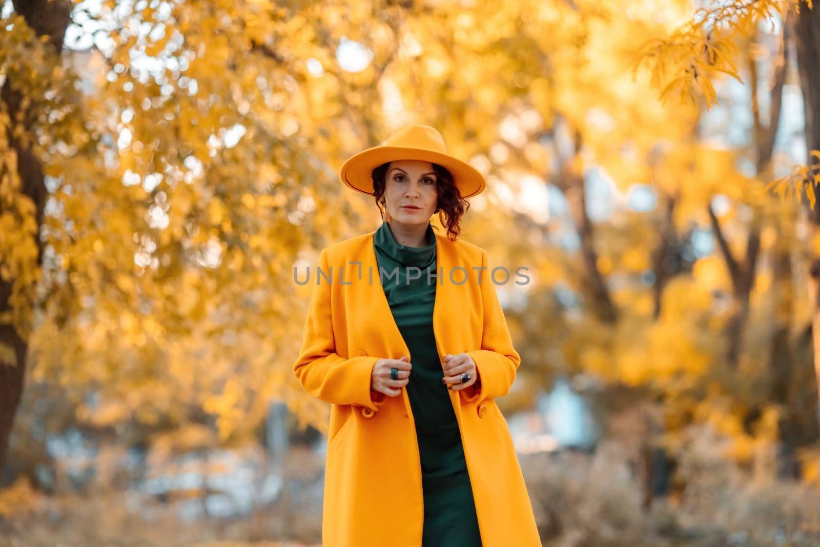 Beautiful woman walks outdoors in autumn. She is wearing a yellow coat, yellow hat and green dress. Young woman enjoying the autumn weather. Autumn content by Matiunina