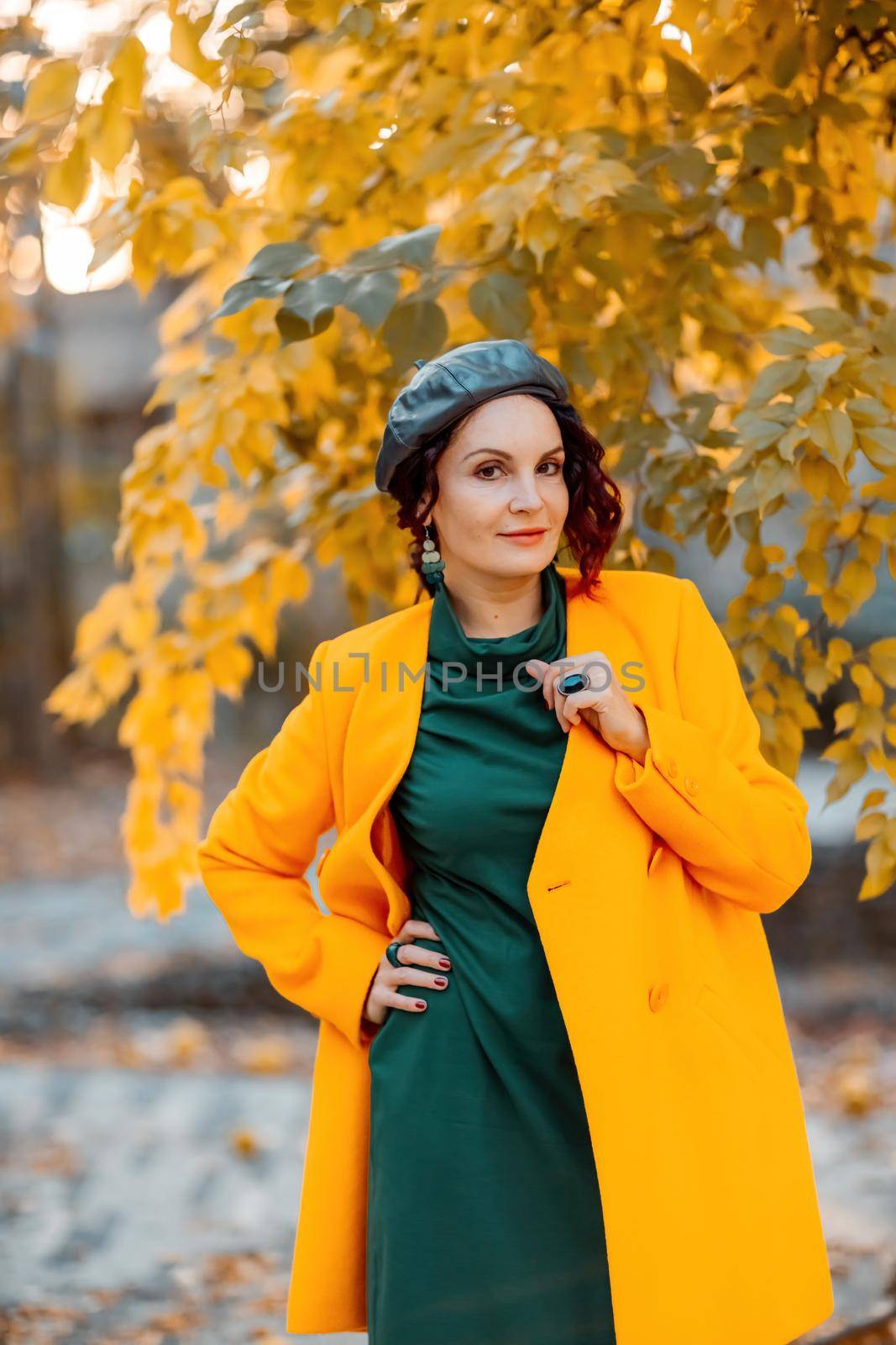 Beautiful woman walks outdoors in autumn. She is wearing a yellow coat and a green dress. Young woman enjoying the autumn weather. Autumn content