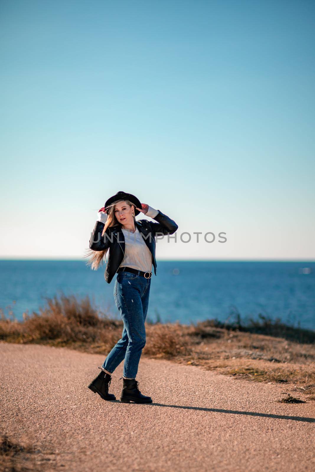 A blonde in a stylish black leather jacket walks along the seashore