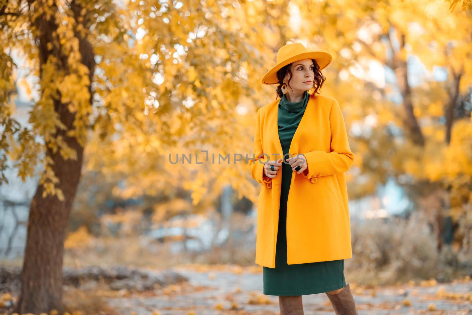 Beautiful woman walks outdoors in autumn. She is wearing a yellow coat, yellow hat and green dress. Young woman enjoying the autumn weather. Autumn content by Matiunina