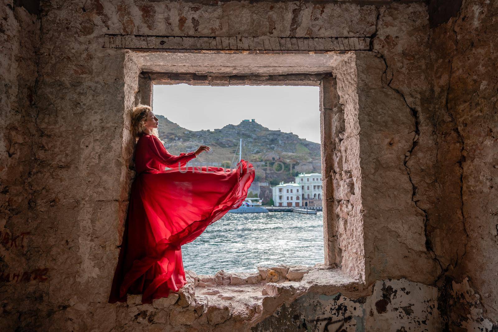 View of Balaklava Bay through an arched balcony in oriental style. The girl in a long red dress stands with her back. Abandoned mansion on the Black Sea coast by Matiunina