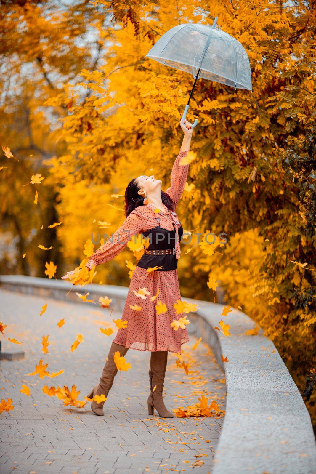 Beautiful girl in a dress with an umbrella in the autumn park. She holds him over her head, autumn leaves are falling out of him.
