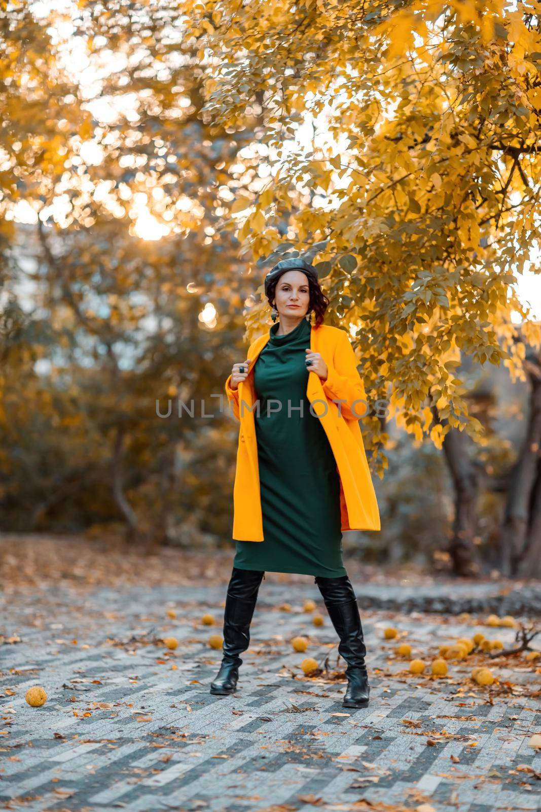 Beautiful woman walks outdoors in autumn. She is wearing a yellow coat and a green dress. Young woman enjoying the autumn weather. Autumn content. by Matiunina