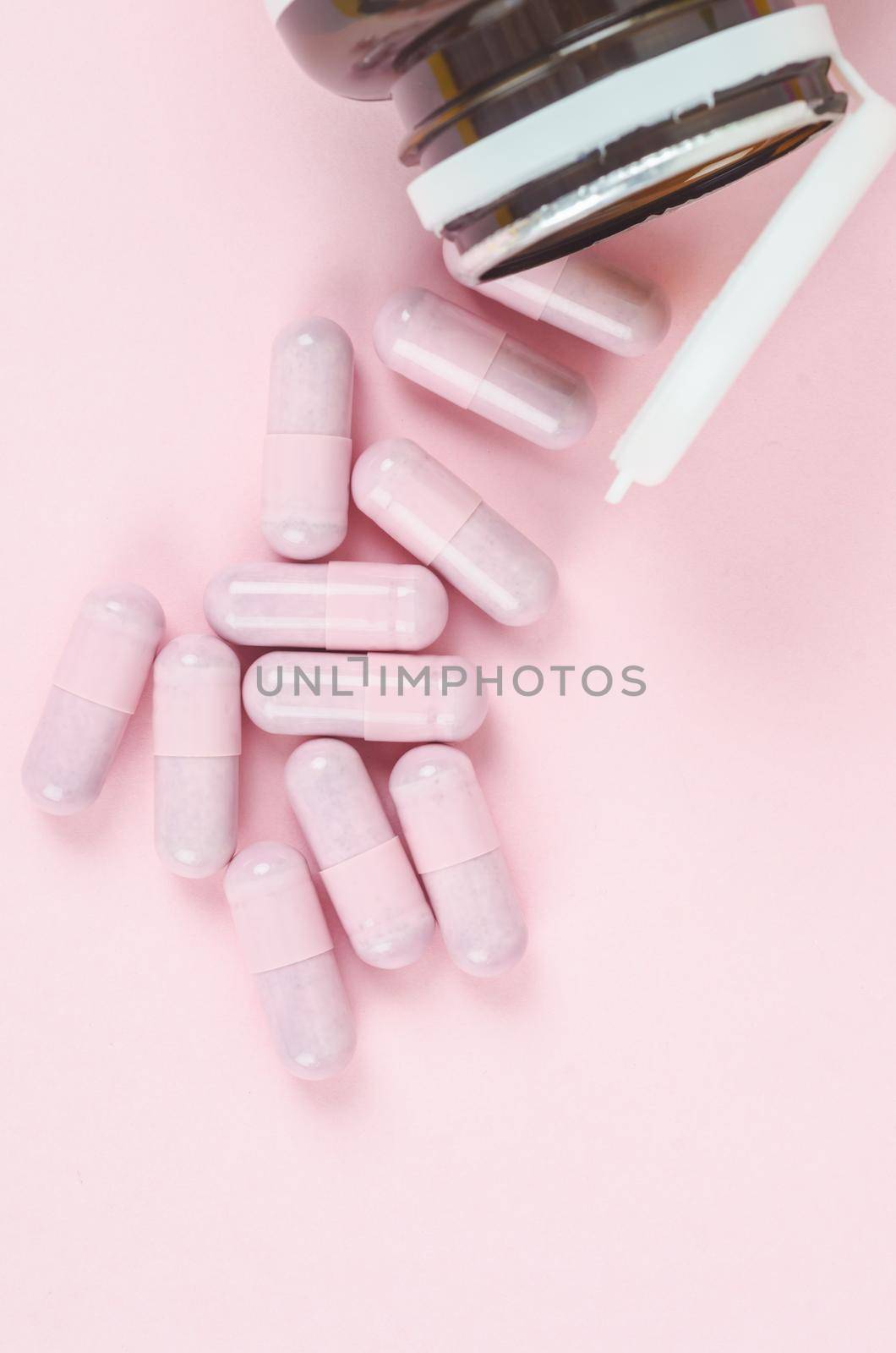 Pink capsule pills with bottle on pink background by Gamjai