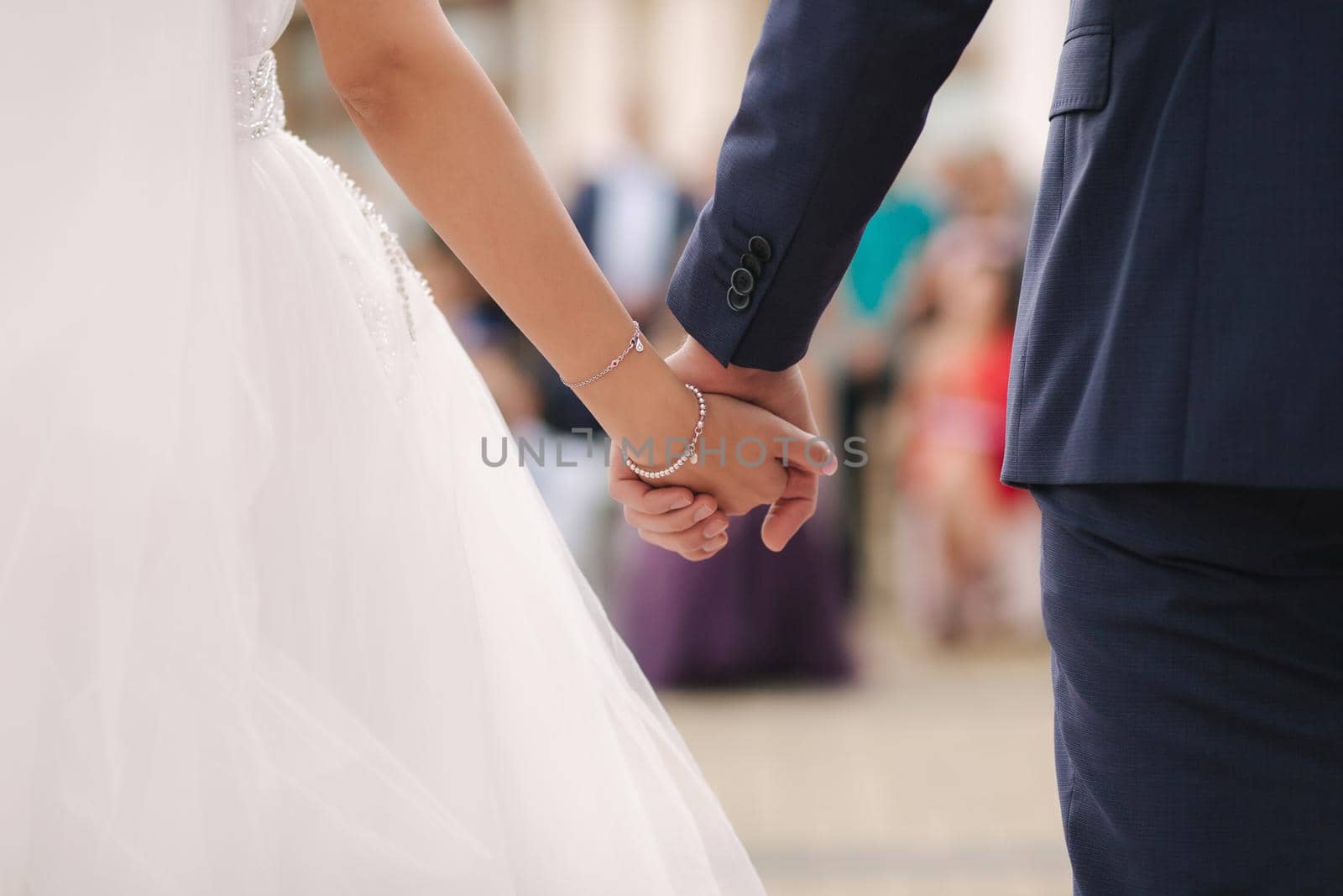 Close up of groom hold bride's hand in front of guests. Wedding ceremony. Back view by Gritsiv