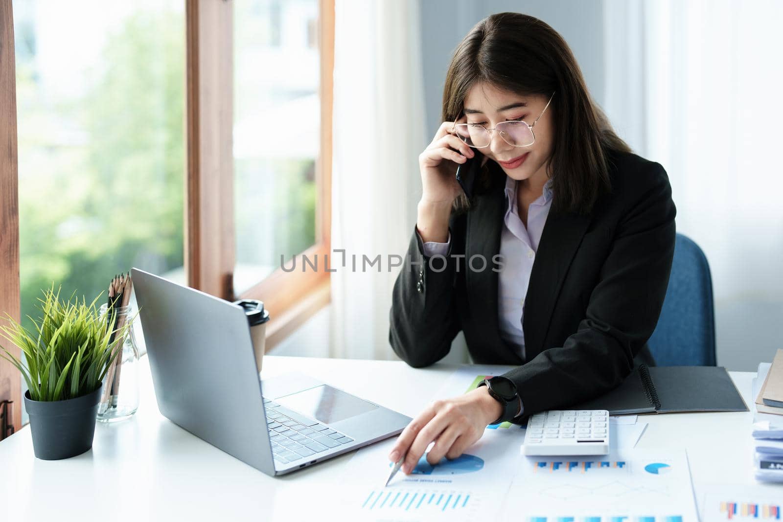 Business correspondence, consultation, portrait of an Asian woman on the phone talking and planning financial statements and investments and using computers and documents to analyze financial systems. by Manastrong