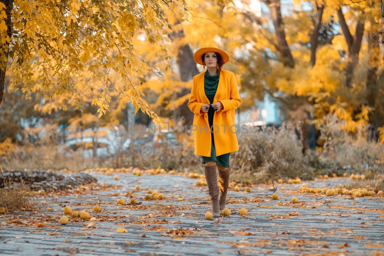 Beautiful woman walks outdoors in autumn. She is wearing a yellow coat, yellow hat and green dress. Young woman enjoying the autumn weather. Autumn content.