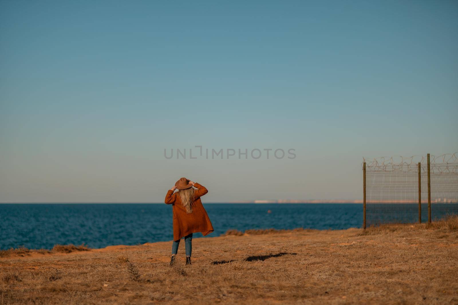 A woman walking along the coast near the sea. An elegant lady in a brown coat and a hat with fashionable makeup walks on the seashore by Matiunina