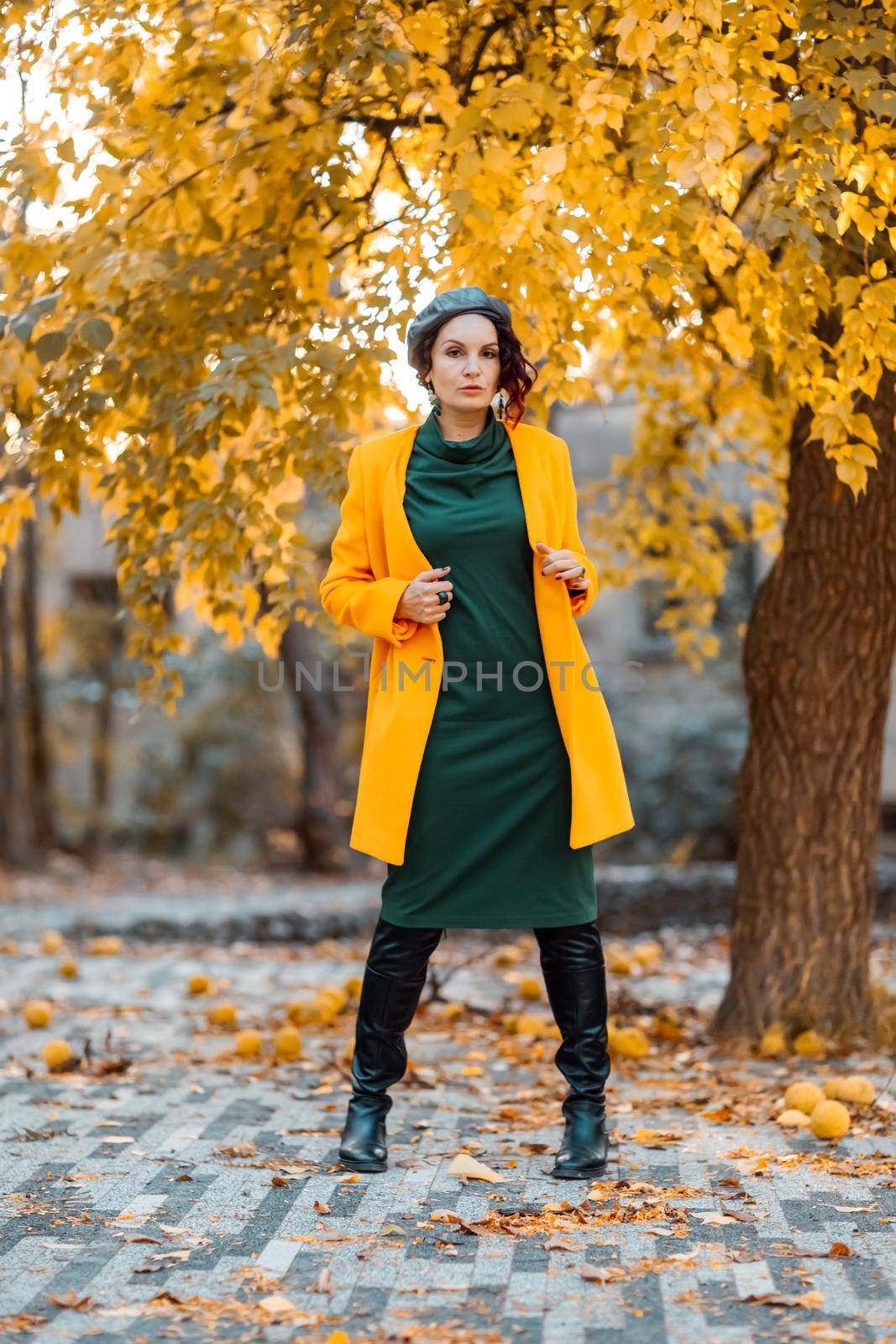 Beautiful woman walks outdoors in autumn. She is wearing a yellow coat and a green dress. Young woman enjoying the autumn weather. Autumn content. by Matiunina