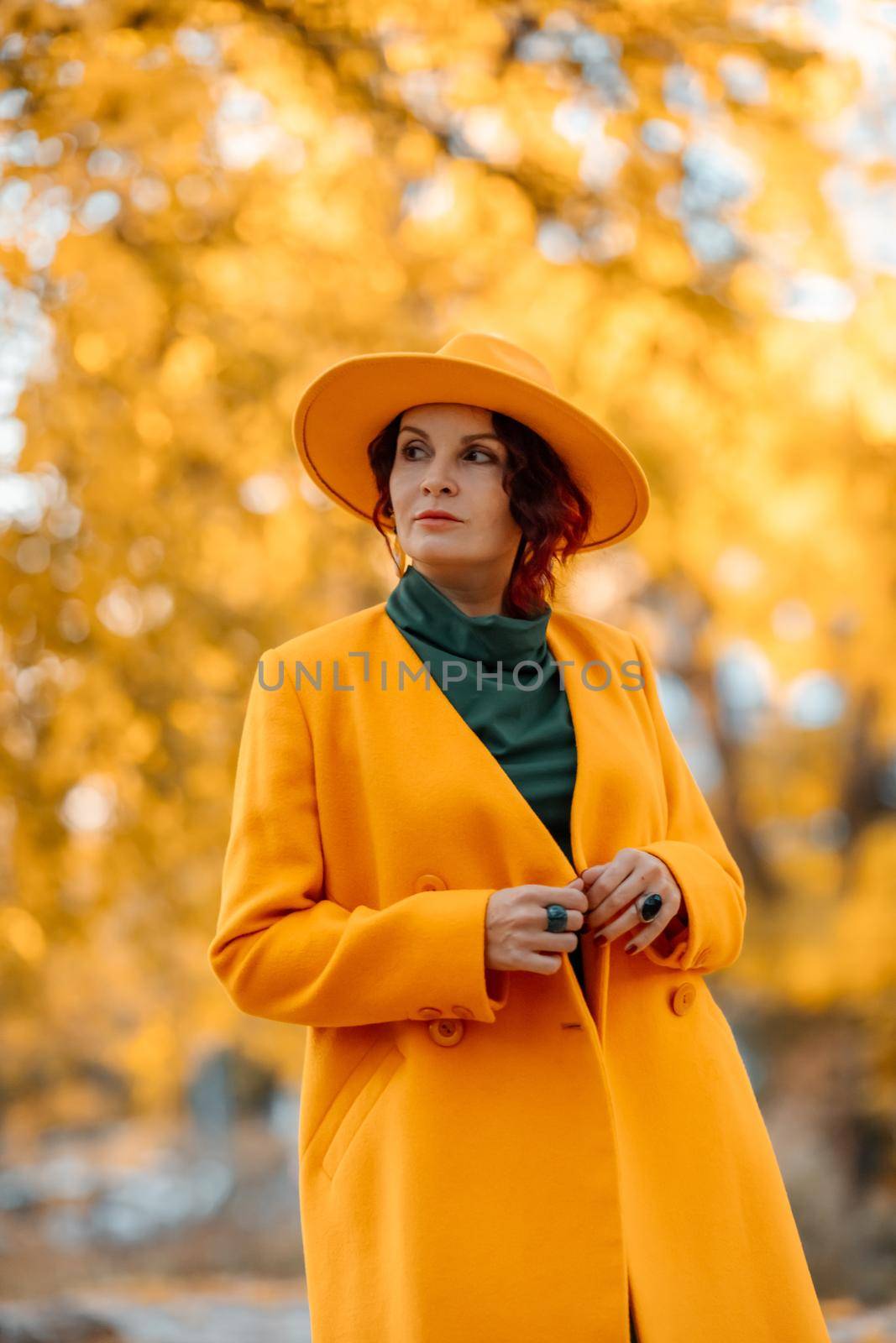 Beautiful woman walks outdoors in autumn. She is wearing a yellow coat, yellow hat and green dress. Young woman enjoying the autumn weather. Autumn content by Matiunina