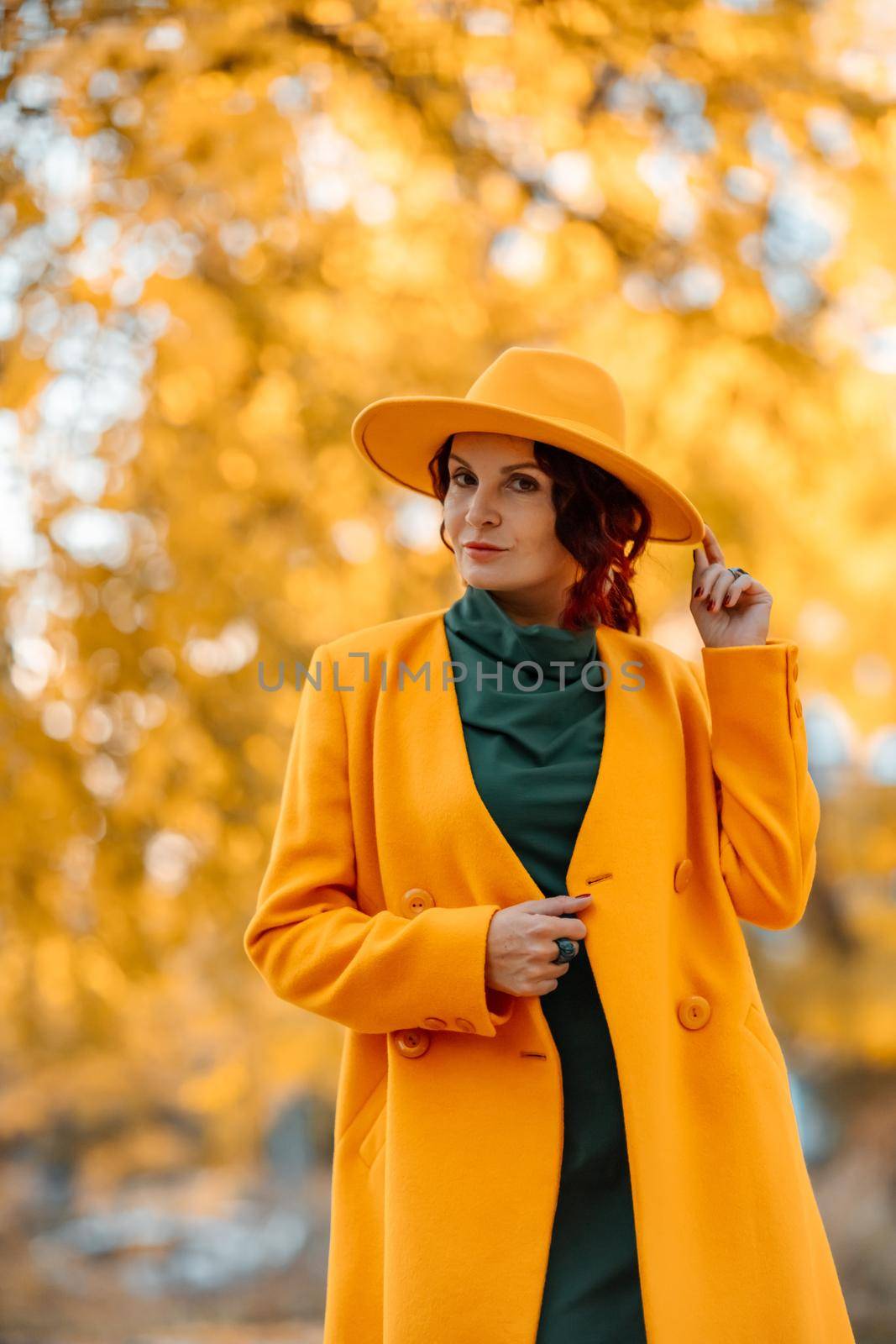 Beautiful woman walks outdoors in autumn. She is wearing a yellow coat, yellow hat and green dress. Young woman enjoying the autumn weather. Autumn content.