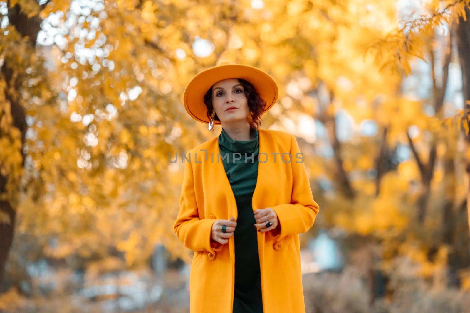 Beautiful woman walks outdoors in autumn. She is wearing a yellow coat, yellow hat and green dress. Young woman enjoying the autumn weather. Autumn content by Matiunina