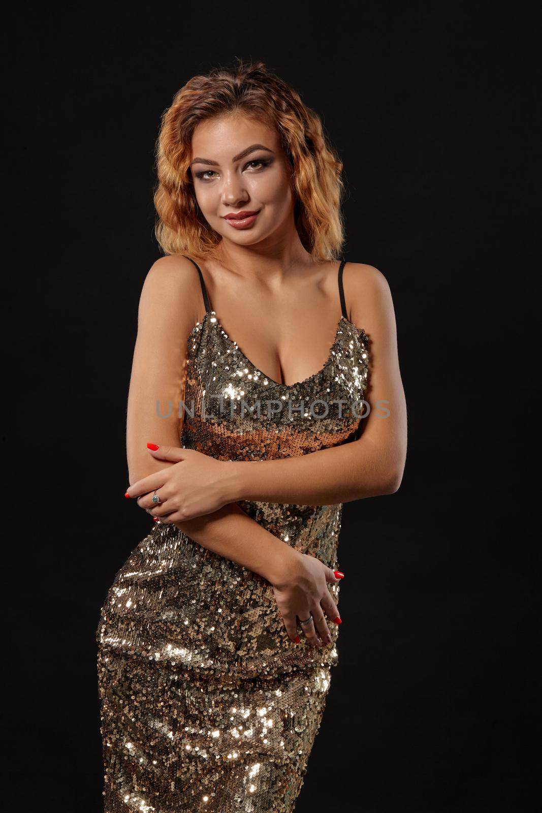 Ginger girl with bright make-up and curly hair, wearing a sexy shiny golden dress is posing standing against a black studio background. Close-up shot. by nazarovsergey