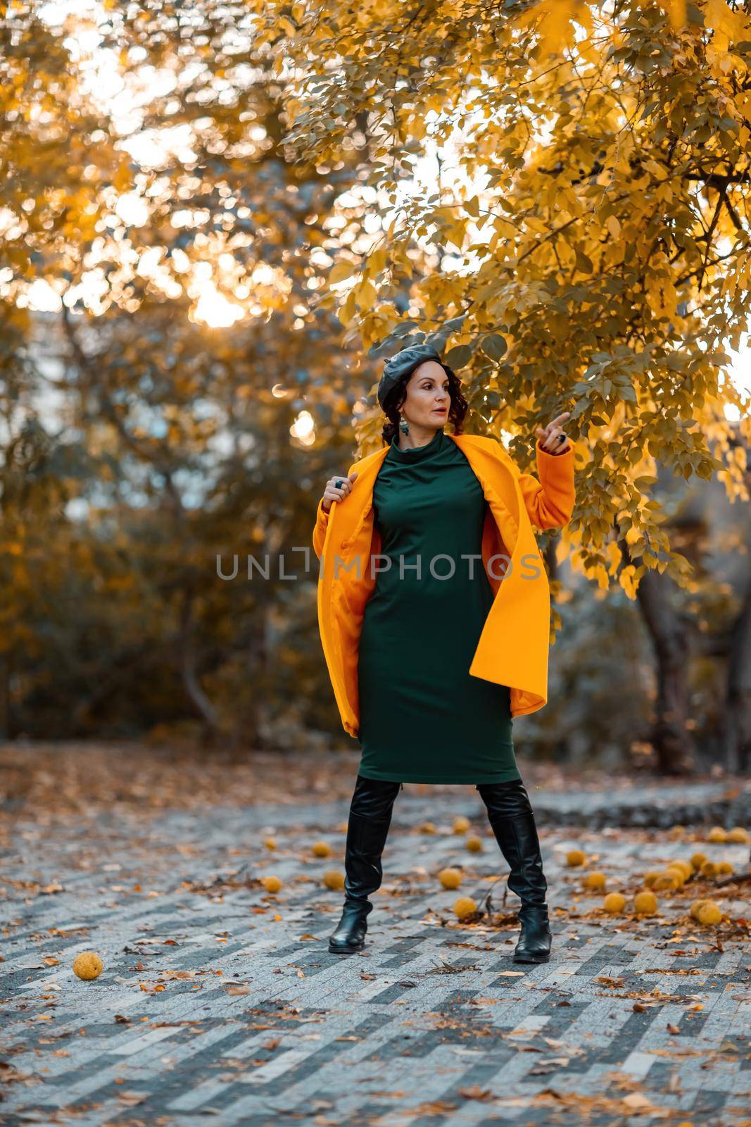 Beautiful woman walks outdoors in autumn. She is wearing a yellow coat and a green dress. Young woman enjoying the autumn weather. Autumn content