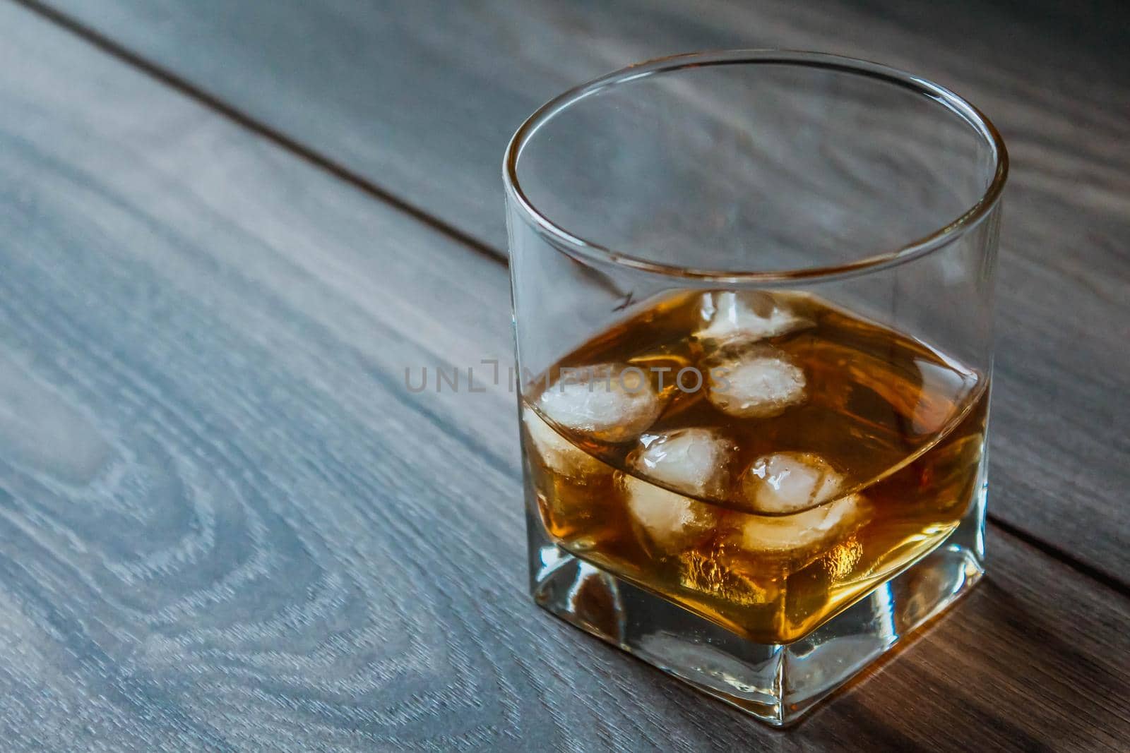Glass with whiskey and ice cubes on a wooden background