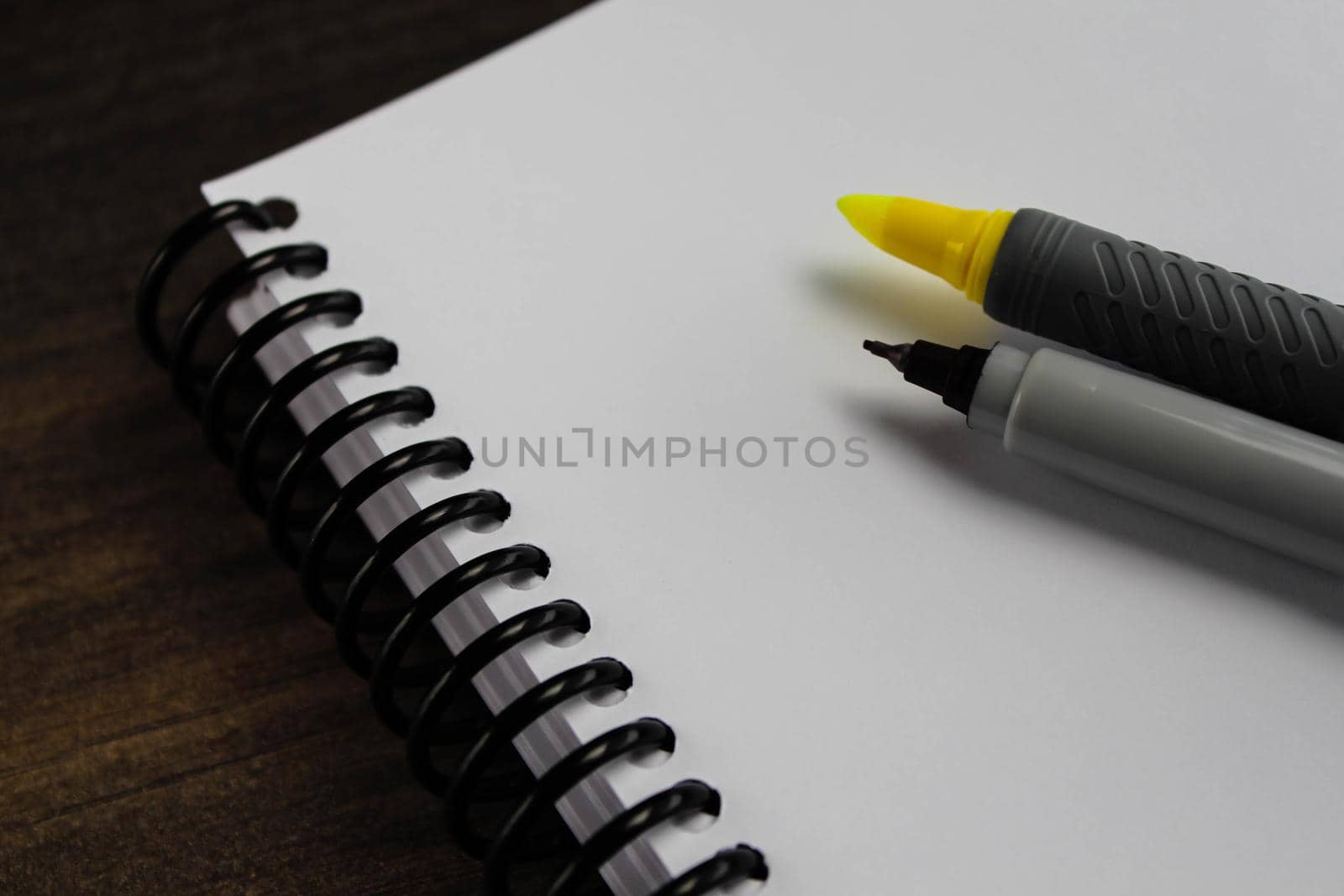 Spiral notepad paper with highlighter and pen on the wooden background. Space for text