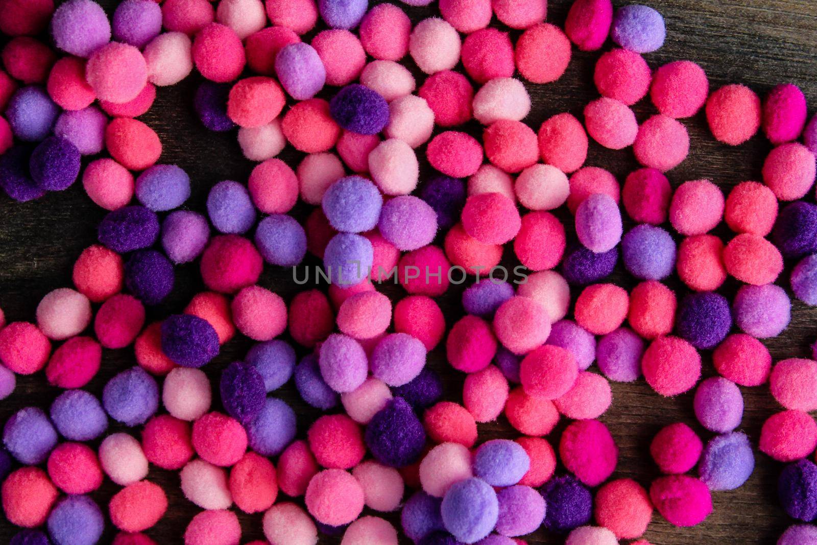 Round pink and purple fluffy balls pompoms on wooden background by JuliaDorian